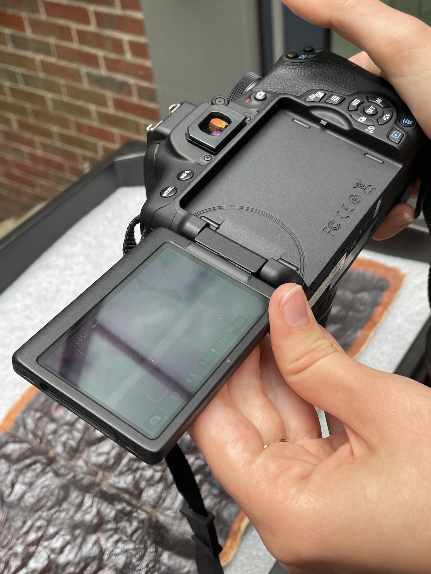 A DSLR camera pointed at a barkcloth, with the infrared preview showing the revealed design.
