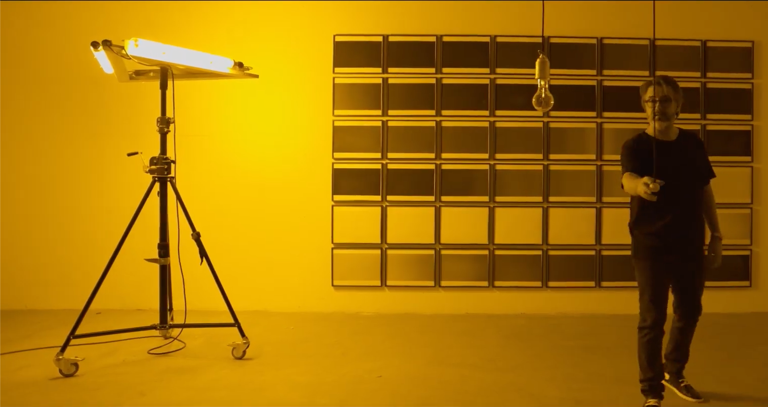 Olafur Eliasson turning on a lightbulb in a room lit with yellow light.